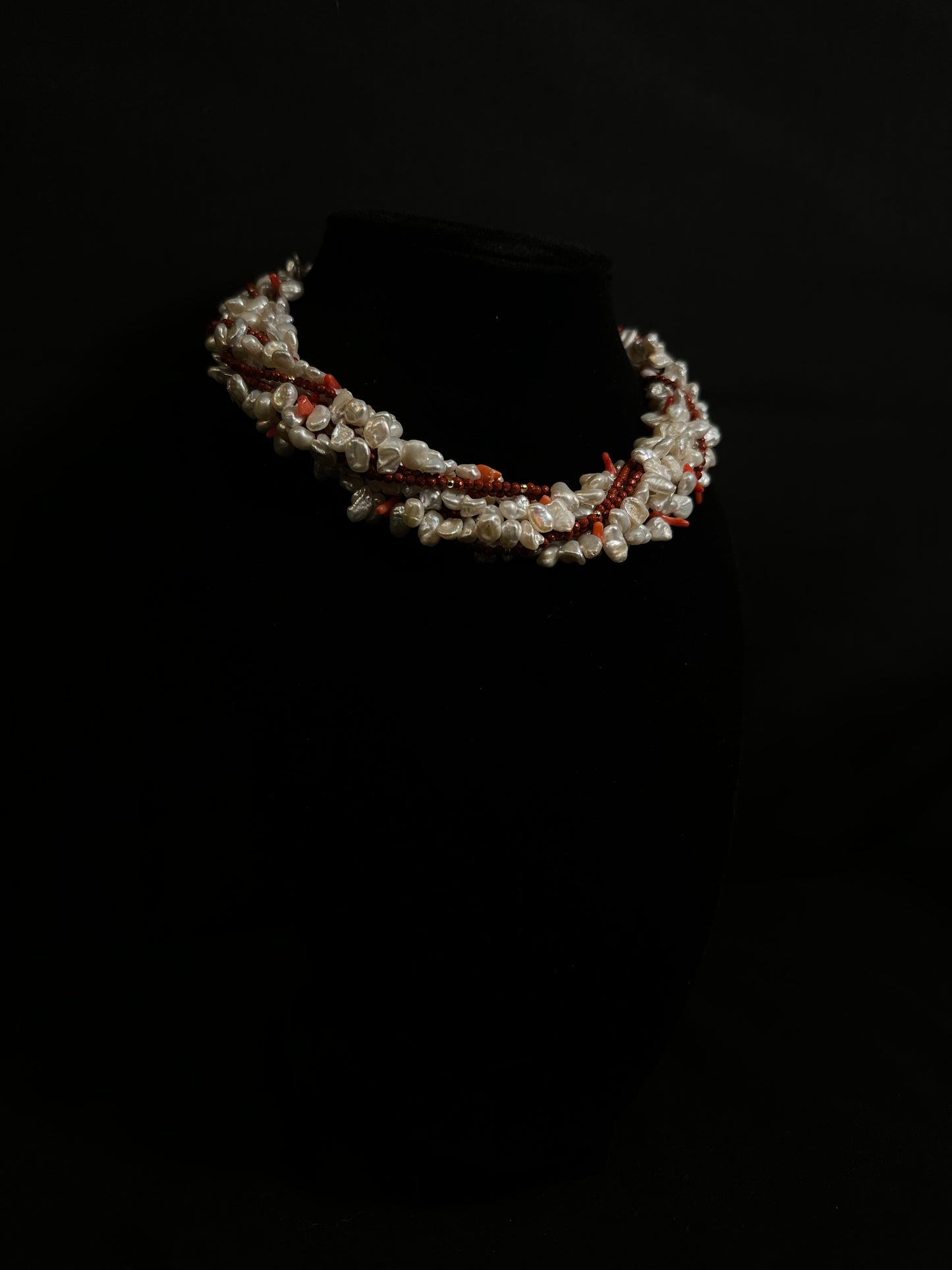 Beaded necklace on a black stand against a dark background