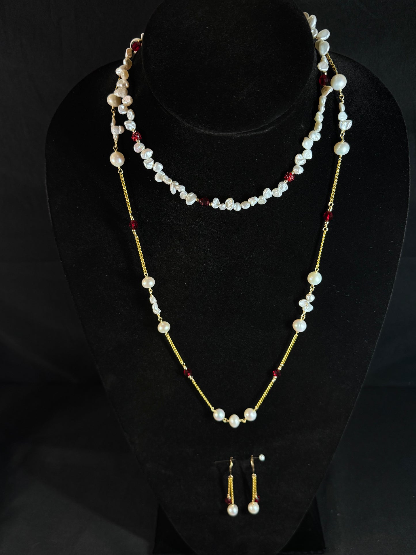 Pearl necklace with red beads and matching earrings on a black background