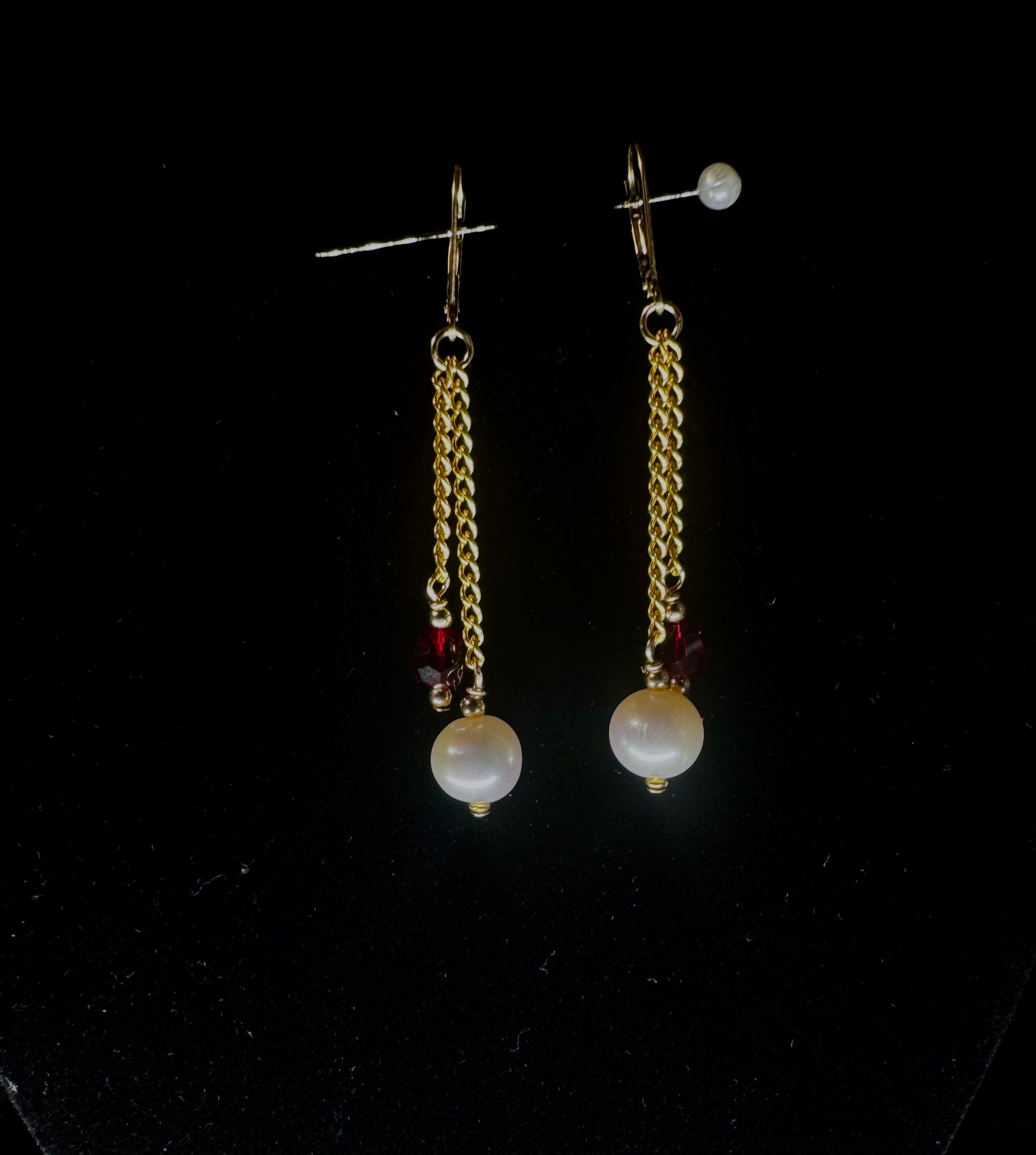 Pair of gold chain earrings with pearl-like beads on a black background