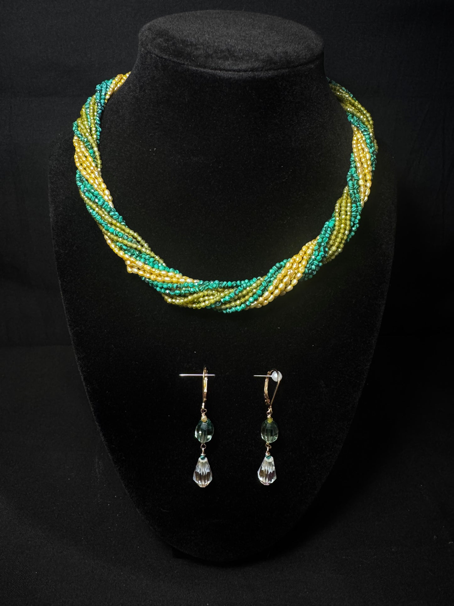 Necklace and earrings set on a black stand with a dark background