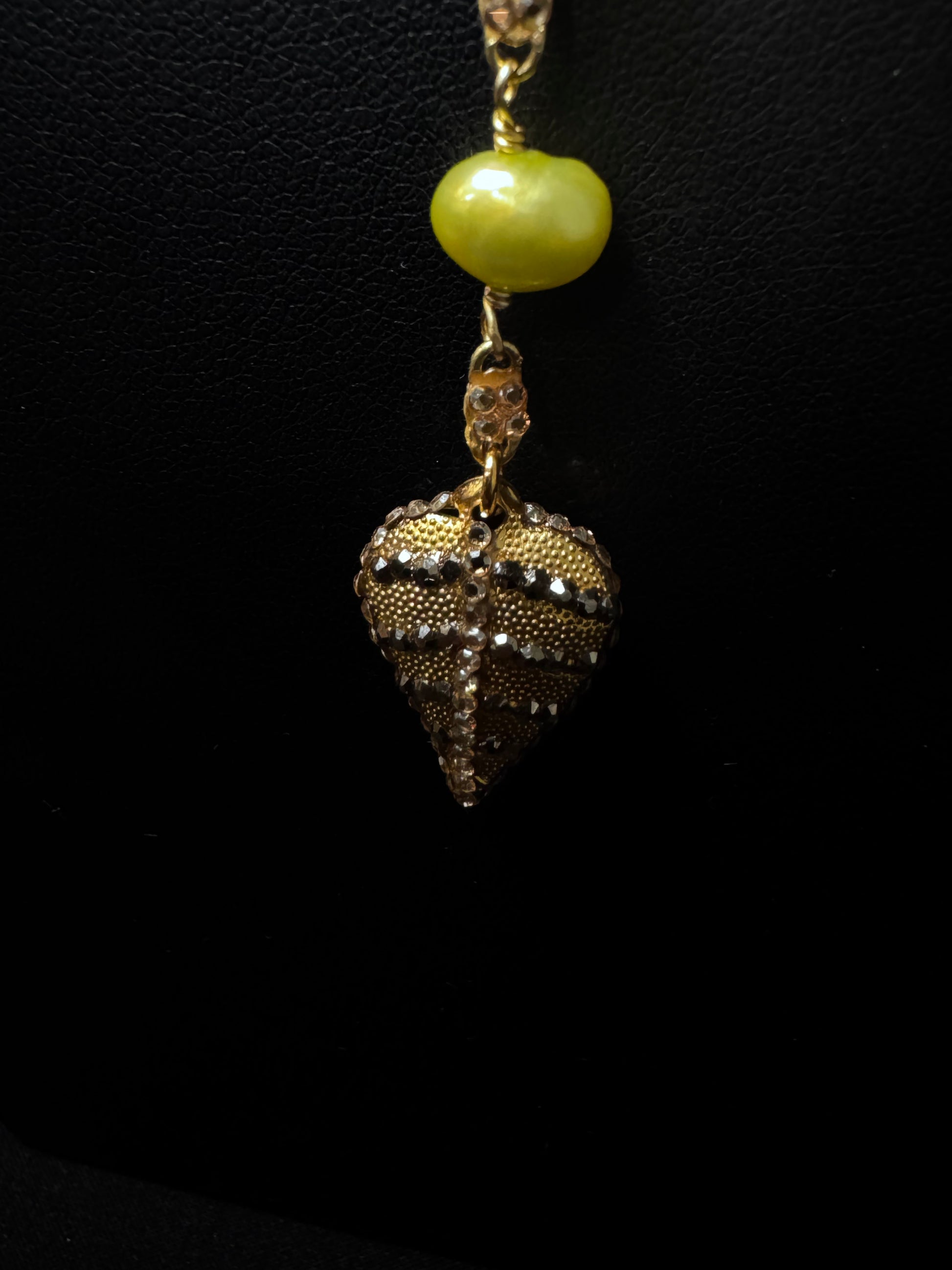 Gold and silver pendant with a green bead on a black background